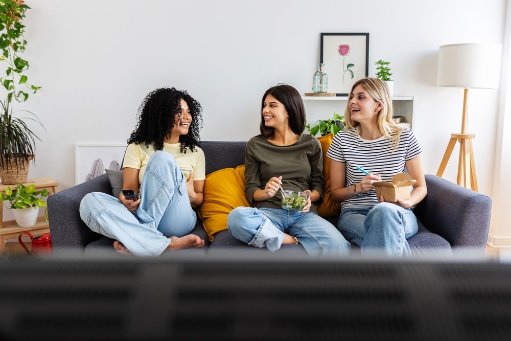 Three college students laughing and talking on couch in their Louisiana apartment, representing renters insurance protection